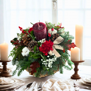 Centro de Navidad pequeño con vela granate, abeto, piñas, ilex, paniculata y lazo beige sobre mesa – Danka Floristas
